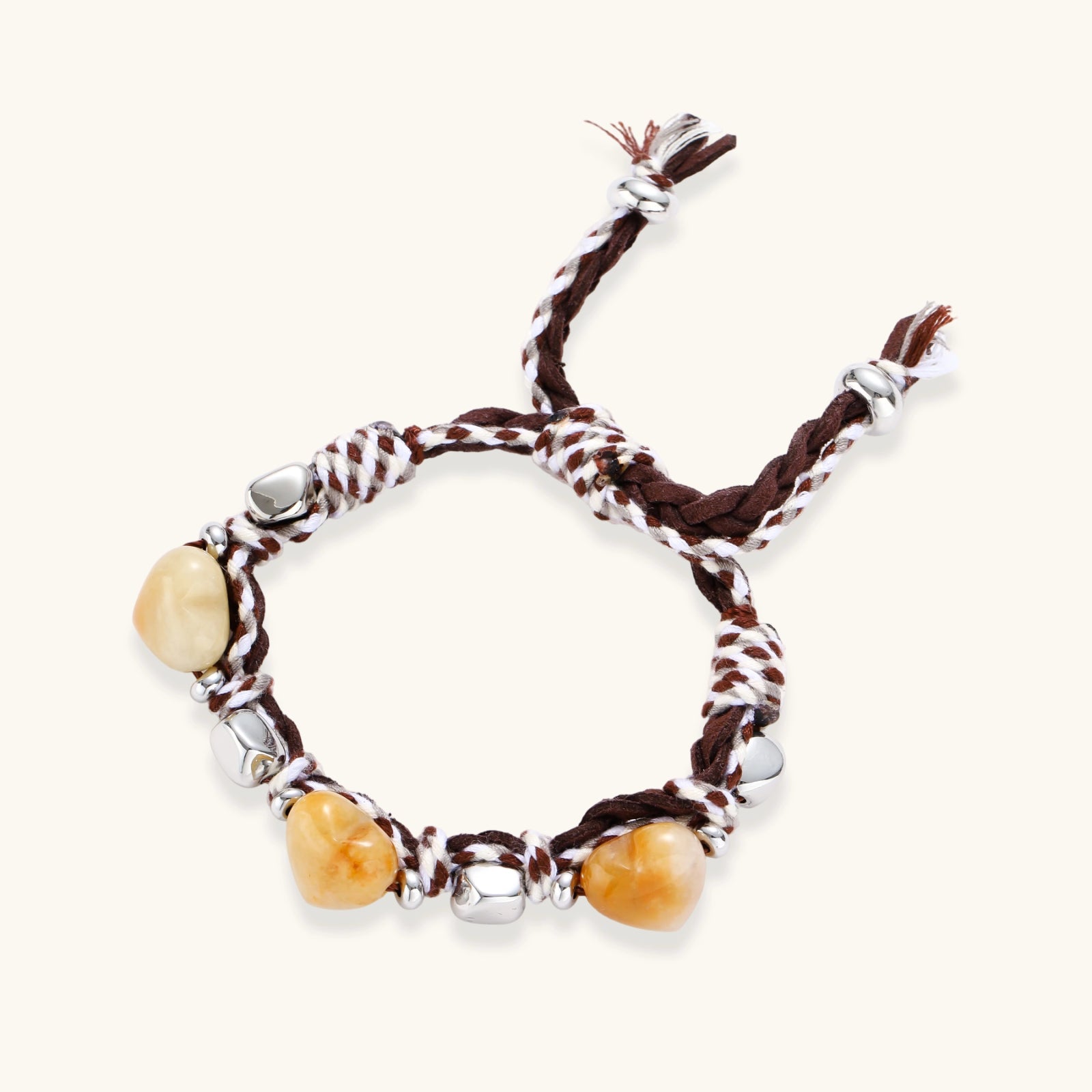 Braided brown and cream suede cord bracelet with heart-shaped amber gemstones and brass beads on white background.