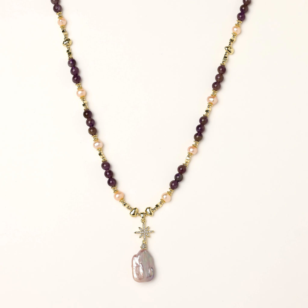 Gold necklace with iridescent baroque pearl pendant, purple amethyst beads, and crystal star charm on cream background