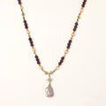 Gold necklace with iridescent baroque pearl pendant, purple amethyst beads, and crystal star charm on cream background