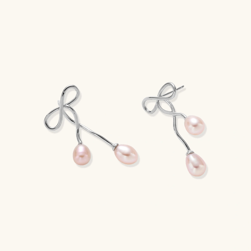Rhodium-plated silver earrings with organic vine curves and two peachy freshwater pearls on cream background